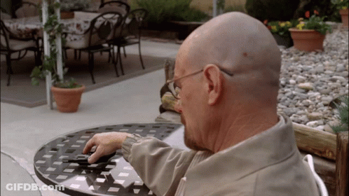 A Bald Man Sits At A Table With A Cell Phone GIF