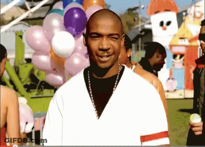 A Bald Man Stands In Front Of A Bunch Of Balloons At A Carnival GIF