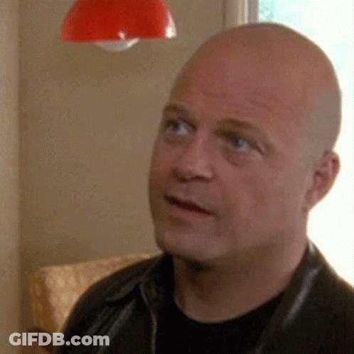 A Bald Man Wearing A Black Shirt And A Black Leather Jacket Is Looking Up At Something . GIF