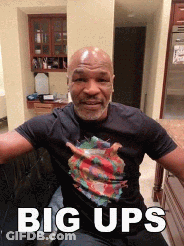 A Bald Man Wearing A Black Shirt With The Words Big Ups On The Bottom GIF