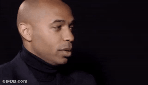 A Bald Man Wearing A Black Turtleneck Is Smiling . GIF