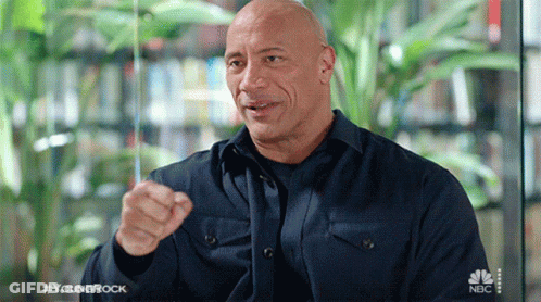 A Bald Man Wearing A Blue Shirt Is Pointing At The Camera . GIF