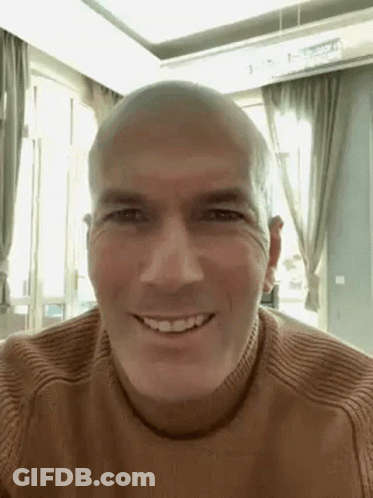 A Bald Man Wearing A Brown Sweater Is Smiling . GIF