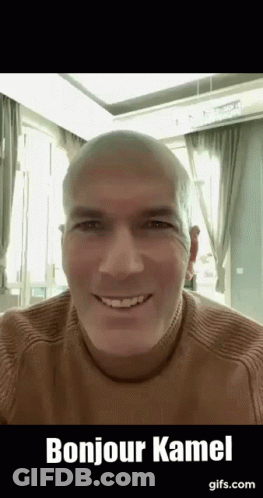 A Bald Man Wearing A Brown Sweater Is Smiling And Saying Bonjour Kamel . GIF