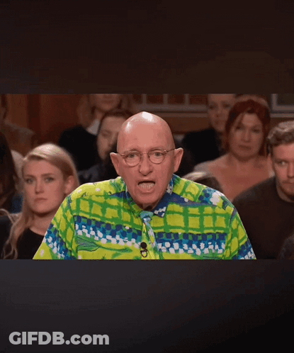 A Bald Man Wearing A Colorful Shirt And Tie Stands In Front Of A Crowd Of People GIF