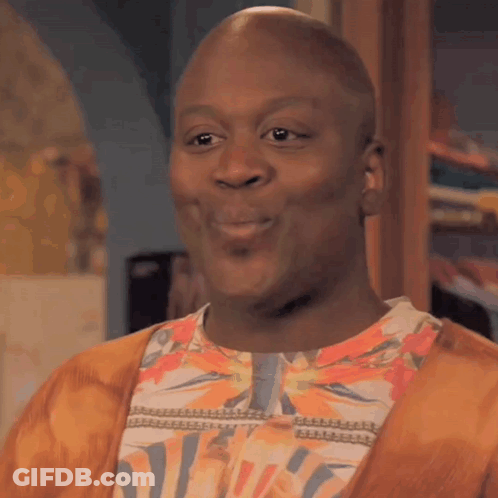 A Bald Man Wearing A Floral Shirt And A Cardigan Is Smiling . GIF