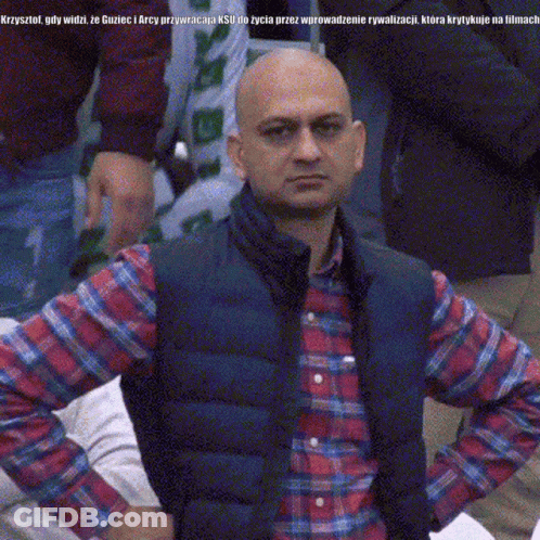 A Bald Man Wearing A Plaid Shirt And A Vest Is Looking At The Camera With His Hands On His Hips GIF