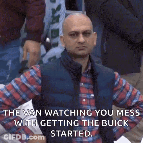 A Bald Man Wearing A Plaid Shirt And Vest Is Standing In A Crowd . GIF
