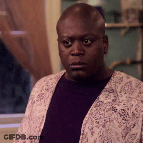 A Bald Man Wearing A Purple Shirt And A White Jacket Looks At The Camera . GIF