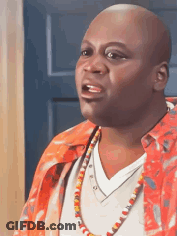 A Bald Man Wearing A Red Shirt And A Necklace Is Talking GIF
