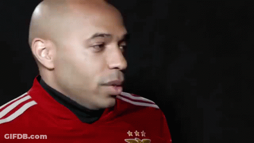 A Bald Man Wearing A Red Shirt With Three Stars On It Is Looking At The Camera . GIF