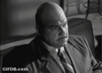 A Bald Man Wearing A Suit And Tie Is Sitting In A Chair GIF