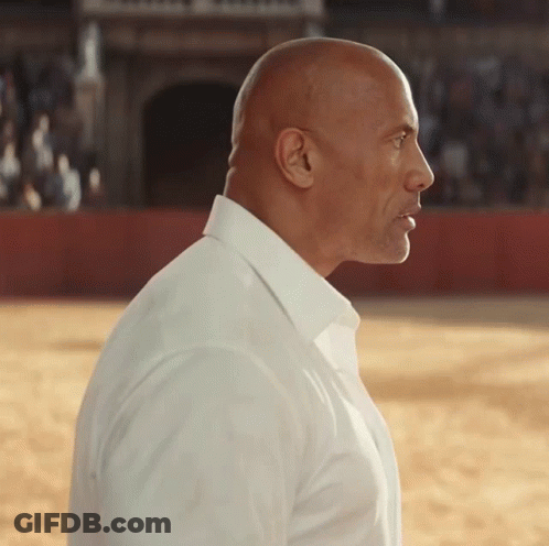 A Bald Man Wearing A White Shirt Stands In A Field GIF