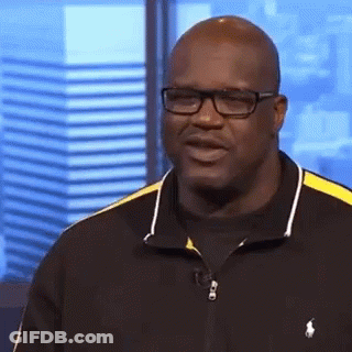 A Bald Man Wearing Glasses And A Black And Yellow Polo Shirt Is Standing In Front Of A Window . GIF