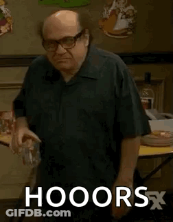 A Bald Man Wearing Glasses And A Black Shirt Is Standing In Front Of A Table And Holding A Glass Of Water . GIF