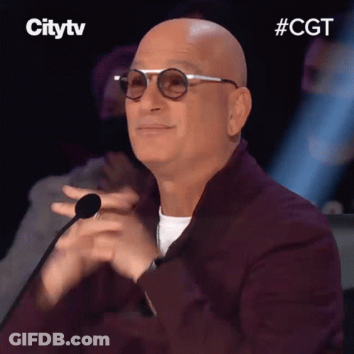 A Bald Man Wearing Glasses And A Burgundy Jacket Is Clapping His Hands In Front Of A Microphone . GIF