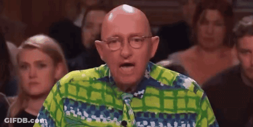 A Bald Man Wearing Glasses And A Green And Blue Shirt Is Speaking In Front Of A Crowd . GIF