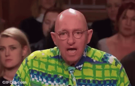 A Bald Man Wearing Glasses And A Green And Blue Shirt Is Speaking In Front Of A Crowd . GIF