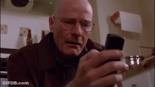 A Bald Man Wearing Glasses Is Looking At A Cell Phone In A Kitchen . GIF