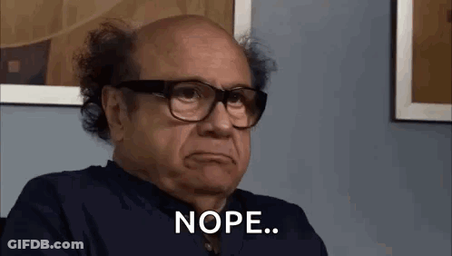 A Bald Man Wearing Glasses Is Sitting In Front Of A Wall And Making A Funny Face . GIF