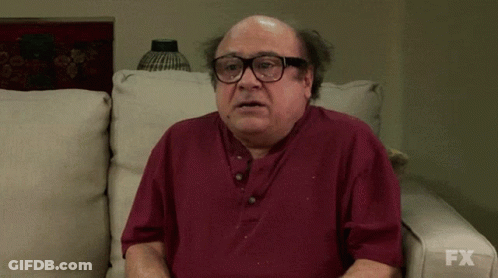 A Bald Man Wearing Glasses Is Sitting On A Couch With Fx Written On The Bottom Of His Shirt GIF