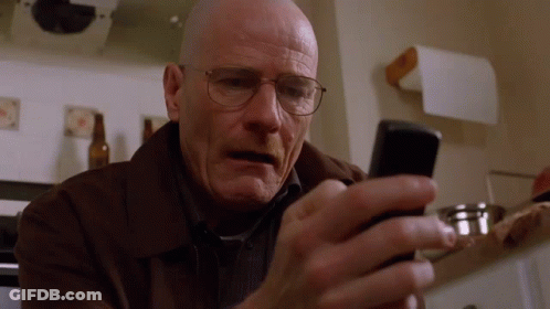 A Bald Man Wearing Glasses Looks At His Cell Phone GIF