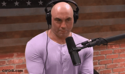 A Bald Man Wearing Headphones And A Purple Shirt Is Sitting In Front Of A Microphone GIF