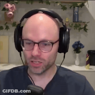 A Bald Man Wearing Headphones And Glasses Is Talking Into A Microphone GIF