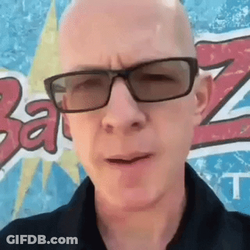A Bald Man Wearing Sunglasses And A Black Shirt Stands In Front Of A Wall With The Letter Z On It GIF