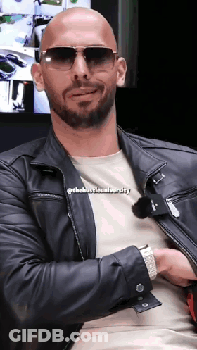A Bald Man Wearing Sunglasses And A Leather Jacket With The Hustle University Written On His Shirt GIF