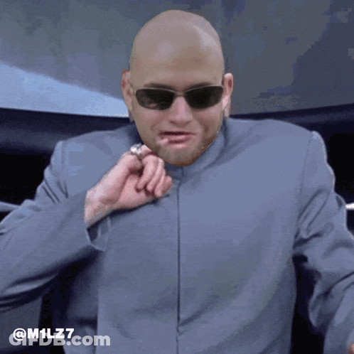 A Bald Man Wearing Sunglasses And A Suit Has The Hashtag M1lz7 On The Bottom GIF