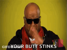 A Bald Man Wearing Sunglasses Is Covering His Mouth With His Hand . GIF