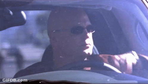 A Bald Man Wearing Sunglasses Is Sitting In A Car . GIF