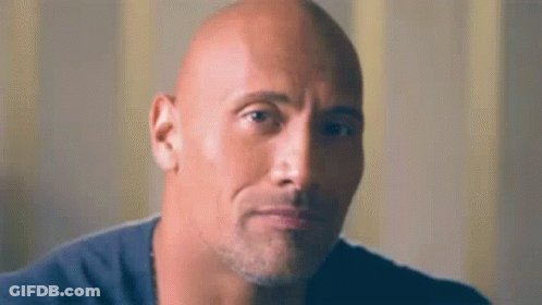 A Bald Man With A Beard And A Blue Shirt Is Looking At The Camera . GIF