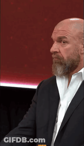 A Bald Man With A Beard And Glasses Is Wearing A Suit And Tie . GIF