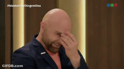 A Bald Man With A Beard Is Covering His Face In Front Of A Masterchef Argentina Logo GIF