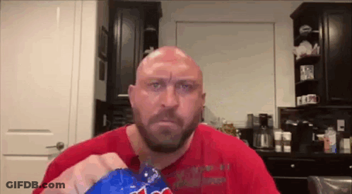 A Bald Man With A Beard Is Eating A Bag Of Potato Chips In A Kitchen . GIF