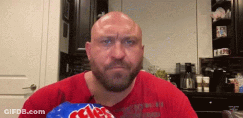 A Bald Man With A Beard Is Holding A Bag Of Chips In His Hand . GIF