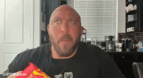 A Bald Man With A Beard Is Holding A Bag Of Chips In His Hand . GIF