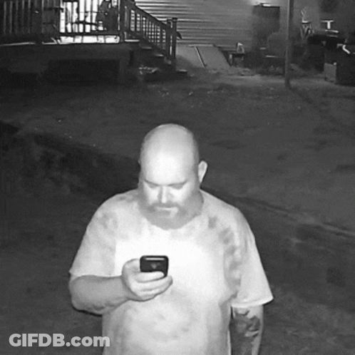 A Bald Man With A Beard Is Holding A Cell Phone GIF