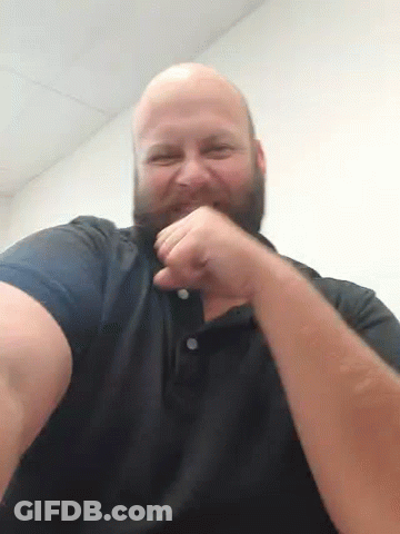A Bald Man With A Beard Is Holding His Fist Up In The Air While Wearing A Black Shirt . GIF