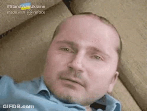 A Bald Man With A Beard Is Laying Down On A Couch . GIF