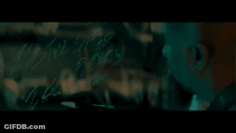 A Bald Man With A Beard Is Looking At Something In A Dark Room GIF