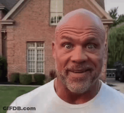 A Bald Man With A Beard Is Making A Face In Front Of A Brick House . GIF