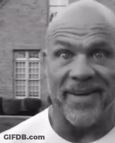 A Bald Man With A Beard Is Making A Funny Face In Front Of A Brick Building GIF