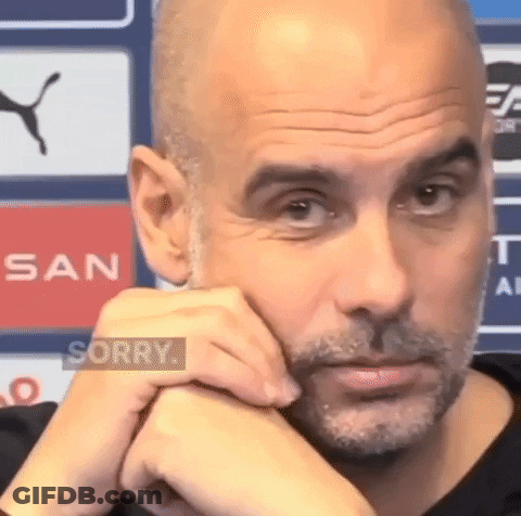 A Bald Man With A Beard Is Sitting With His Hands On His Chin And Looking At The Camera . GIF