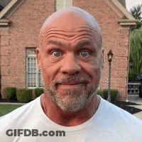 A Bald Man With A Beard Is Standing In Front Of A Brick House And Making A Funny Face . GIF