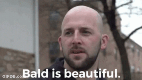 A Bald Man With A Beard Is Standing In Front Of A Building And Says Bald Is Beautiful GIF