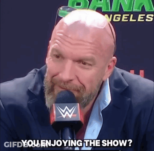 A Bald Man With A Beard Is Talking Into A Microphone With The Words " You Enjoying The Show " Written Below Him GIF