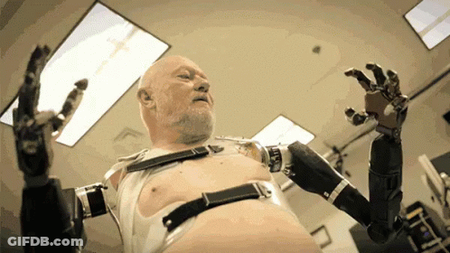 A Bald Man With A Beard Is Wearing A Robot Arm GIF